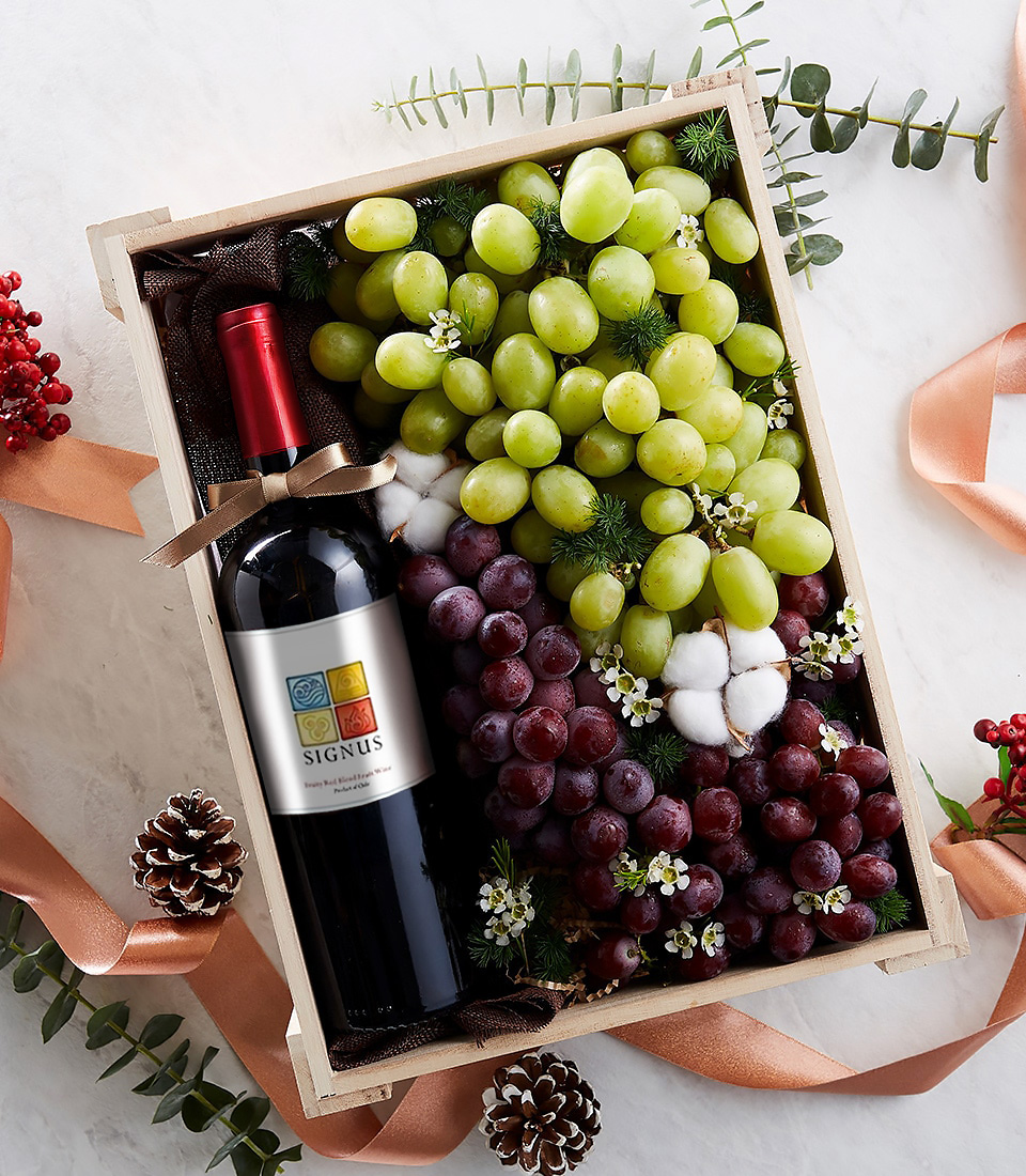 Gift box with Signus red wine, green grapes, red grapes, white flowers, and festive ribbon