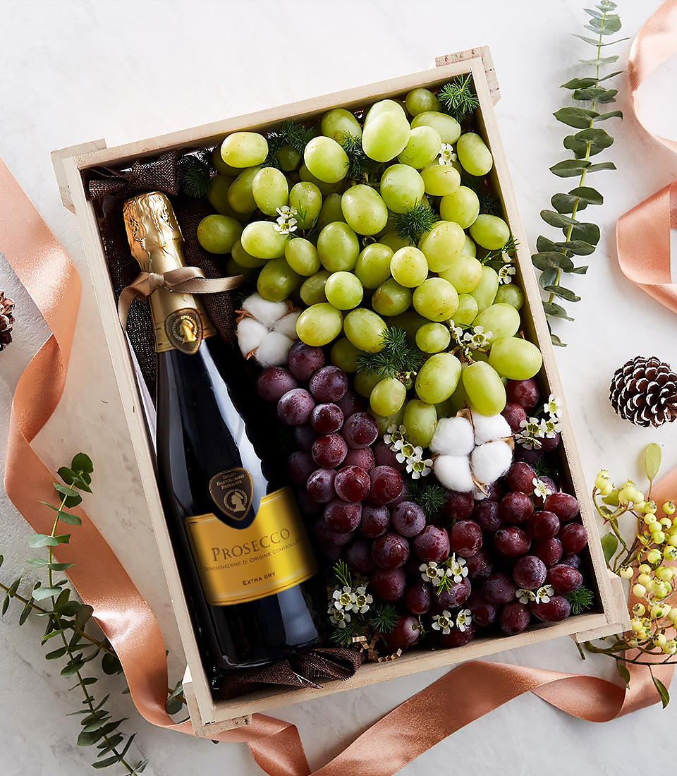 Wooden gift box with Prosecco sparkling wine, green and red grapes, and floral decor