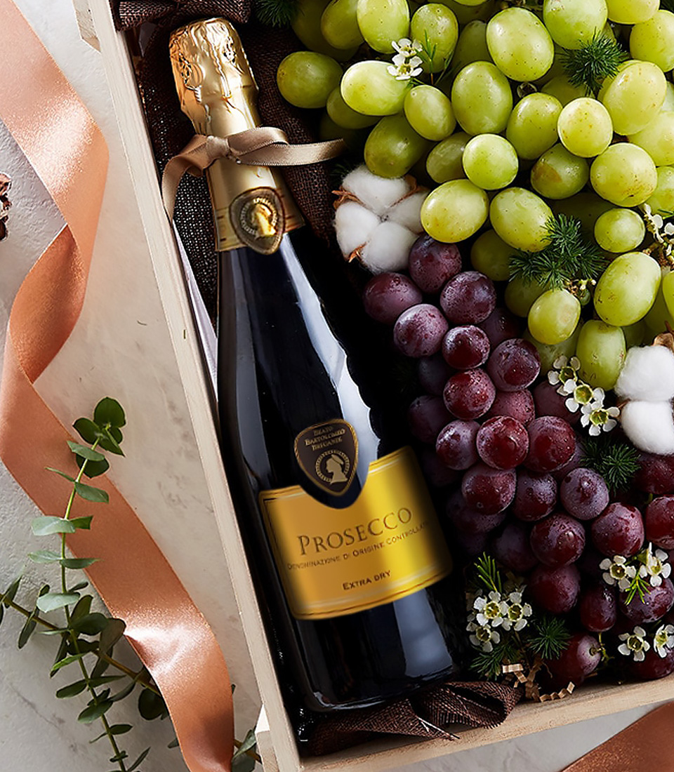 Close-up of Prosecco sparkling wine bottle with green and red grapes in a wooden gift box