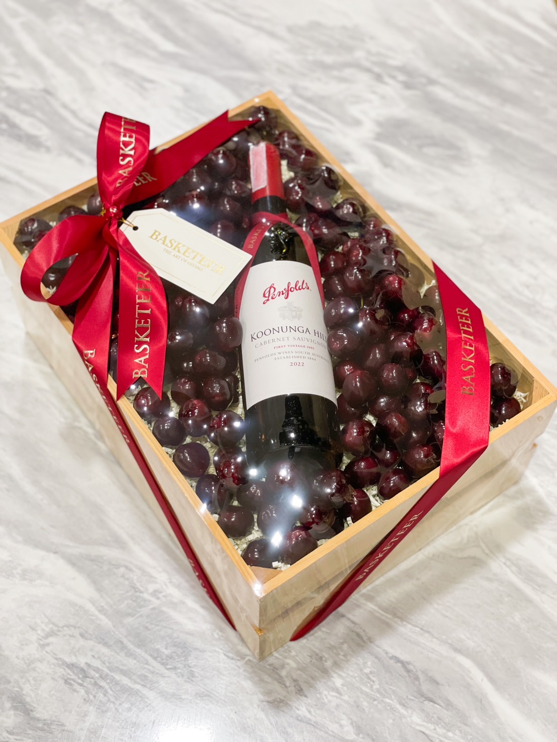 Wooden gift box with fresh cherries and a premium bottle, adorned with a red ribbon by Basketeer.