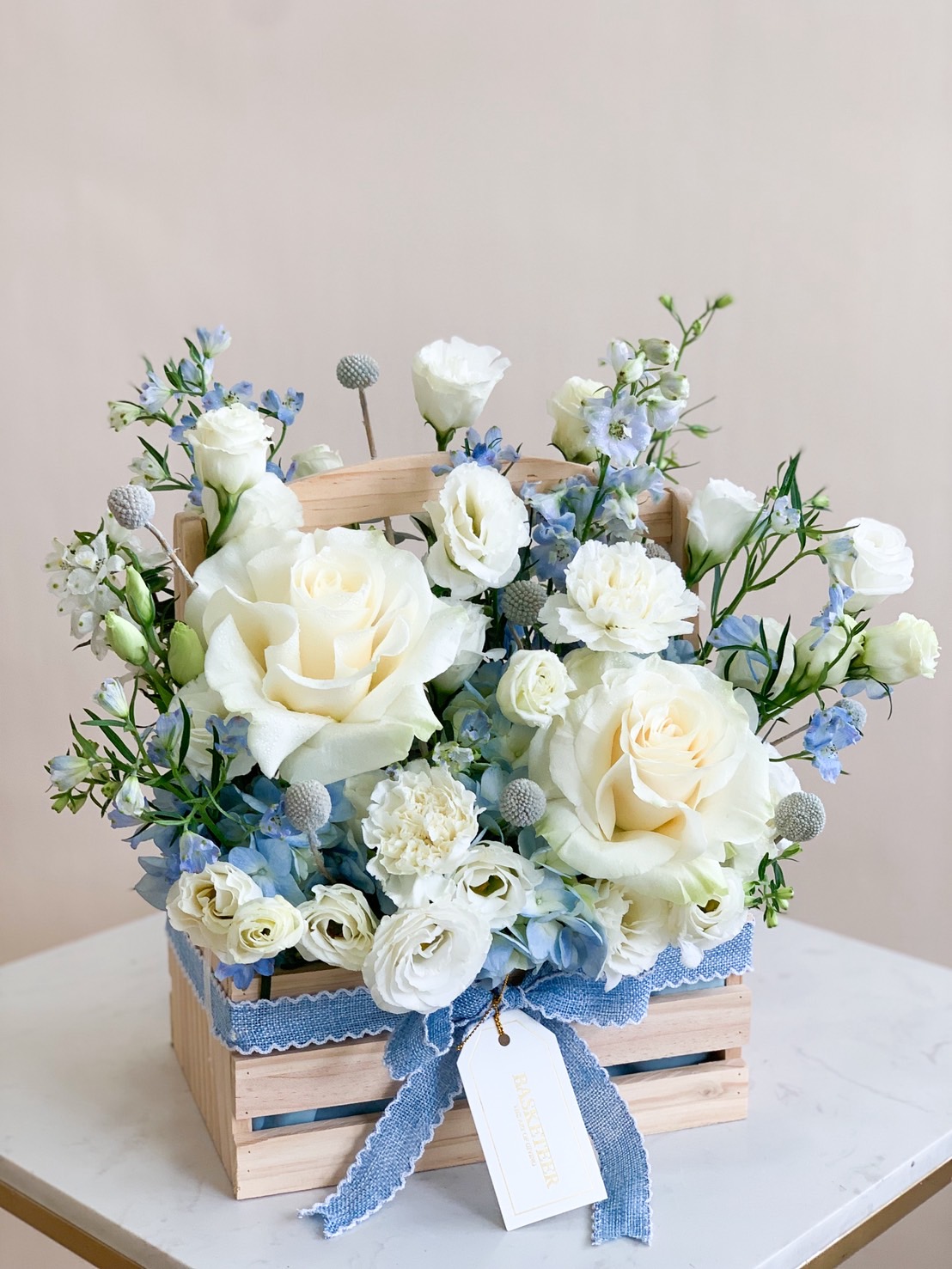 Elegant white and blue fresh flower arrangement in wooden box with roses, hydrangeas, and lisianthus.