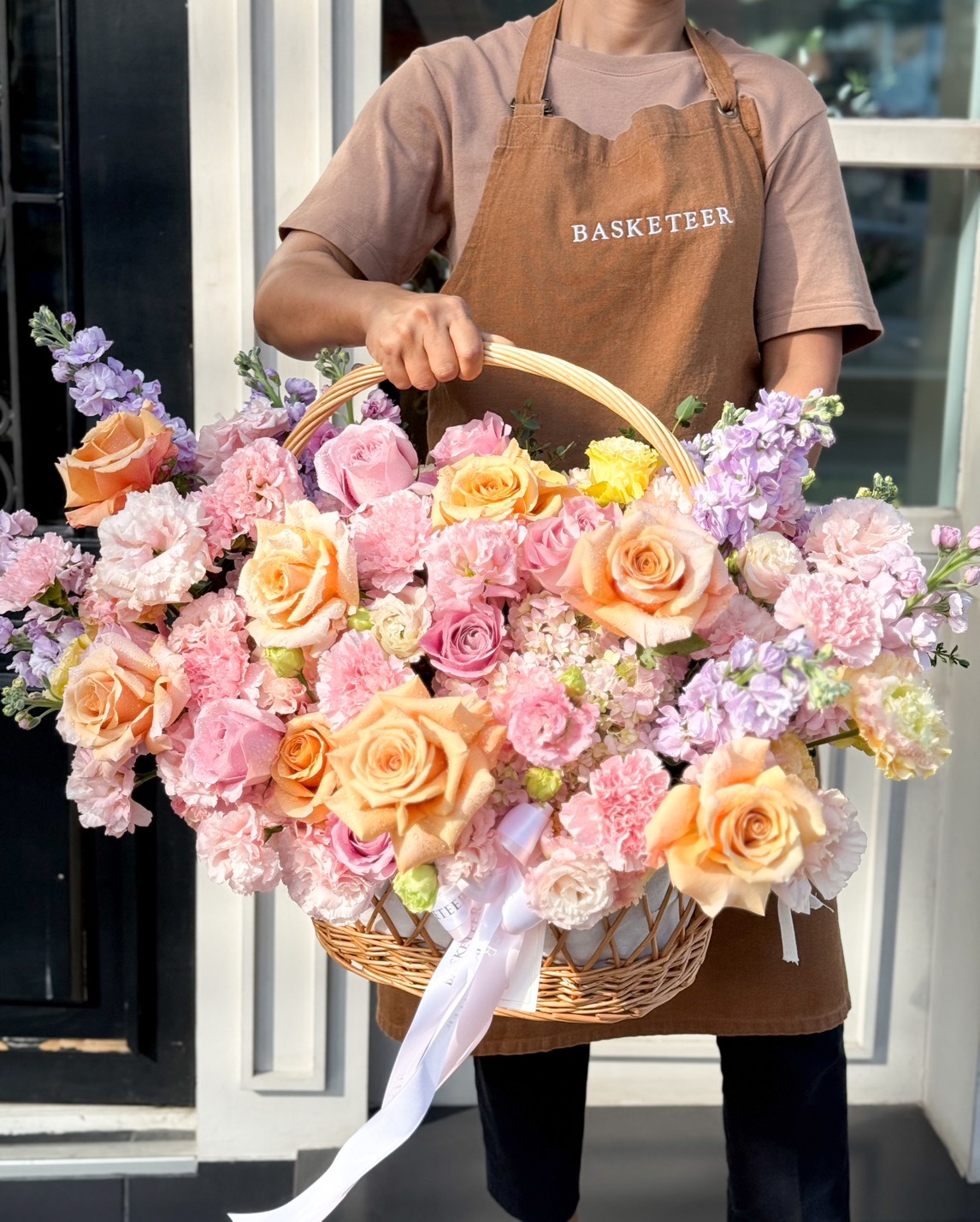 A luxurious handcrafted floral basket filled with pastel roses, hydrangeas, carnations, and stock flowers, elegantly arranged for gifting.