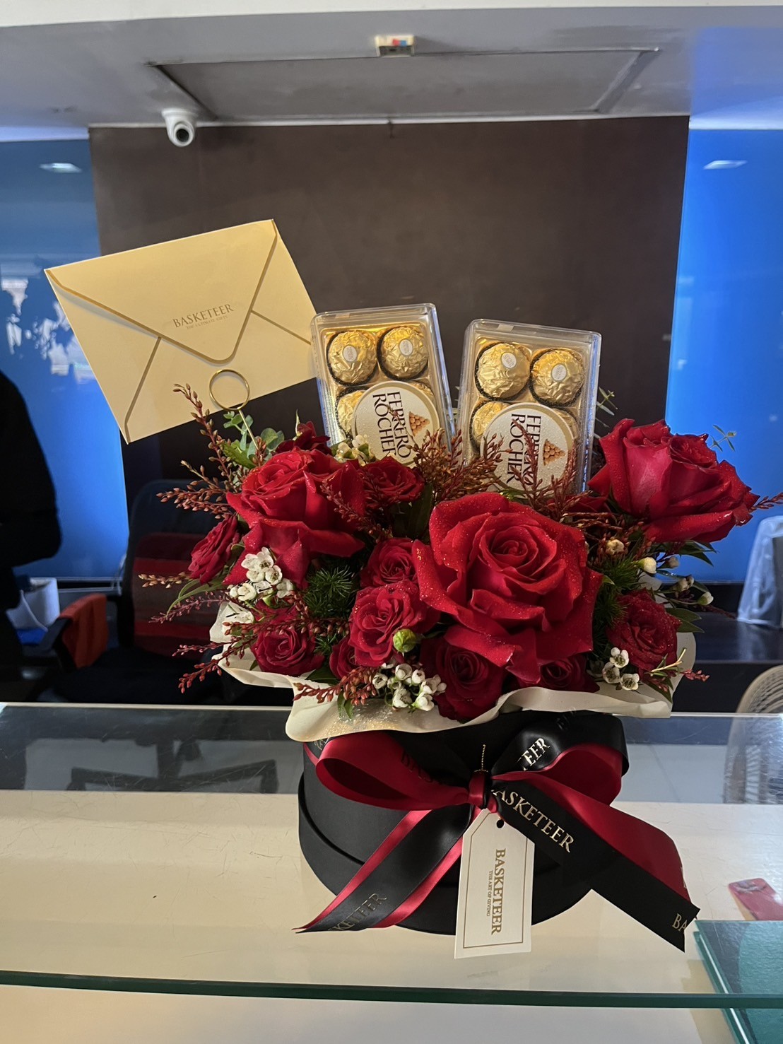 Luxurious round box filled with red roses, Ferrero Rocher chocolates, and festive accents tied with a red satin ribbon.