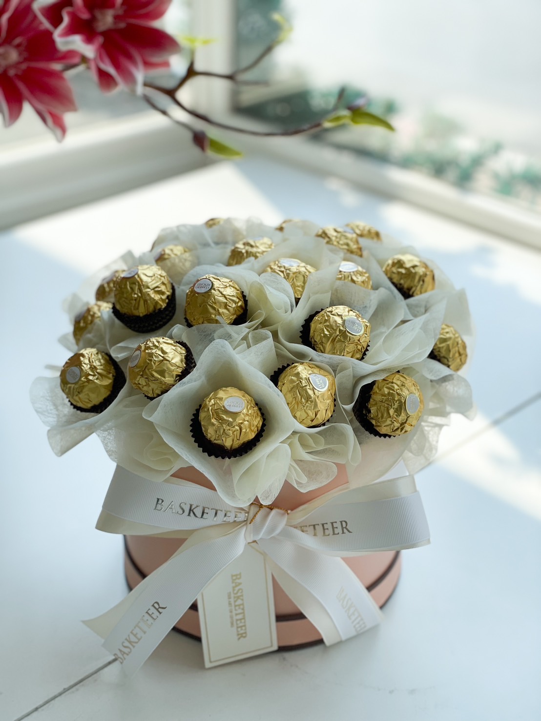 A luxurious Ferrero Rocher chocolate bouquet elegantly arranged in a round gift box with white wrapping and a satin ribbon.