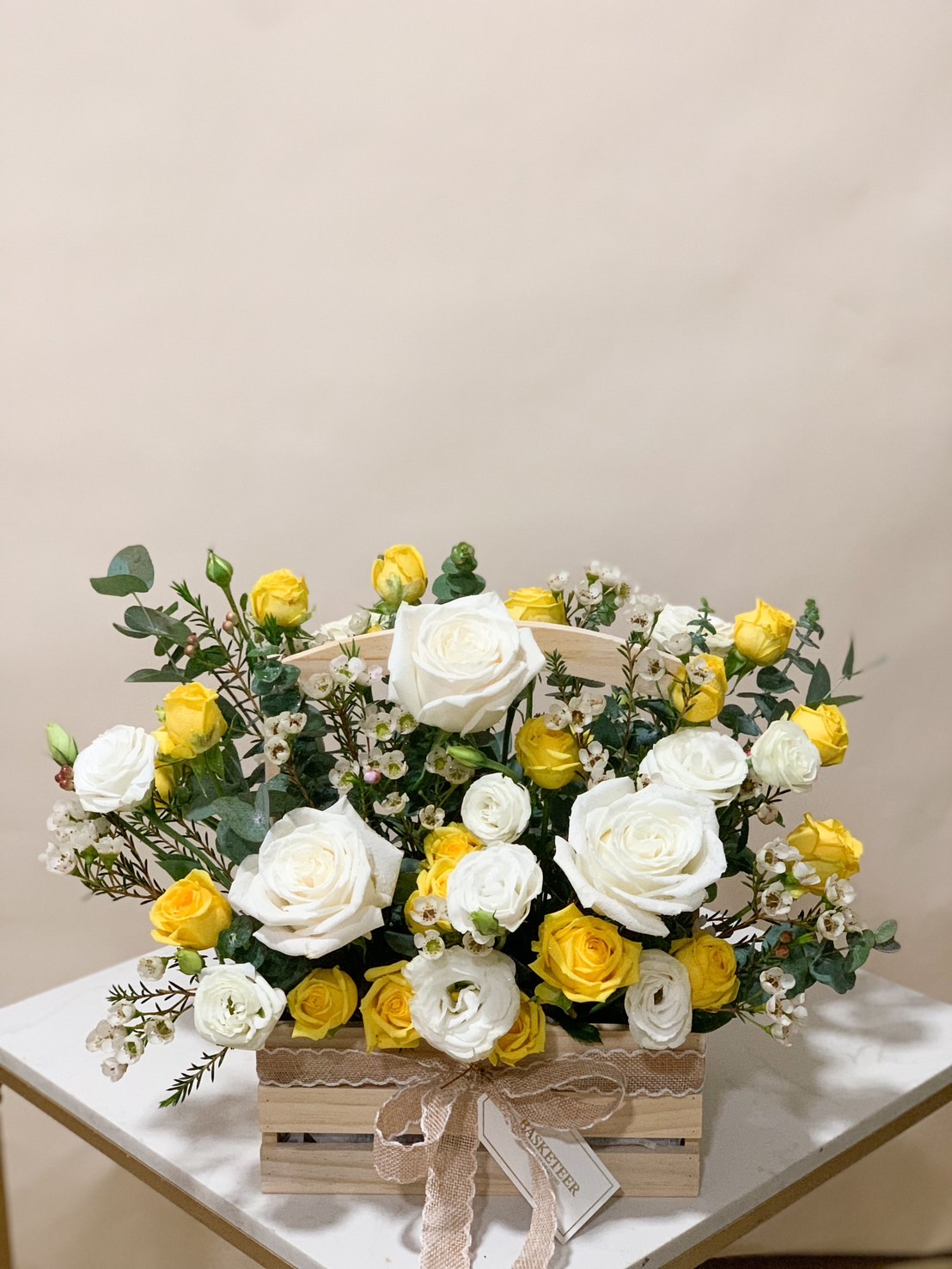 A beautifully arranged yellow and white rose floral basket, featuring fresh blooms with delicate lace ribbon detailing.