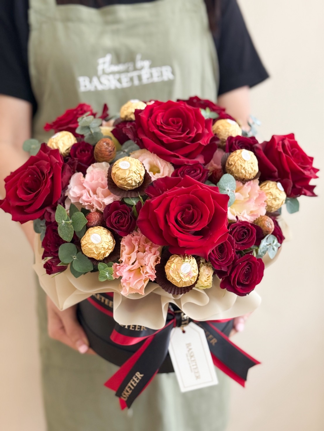 Premium round flower box with red roses, pink carnations, and Ferrero Rocher chocolates in luxurious presentation.