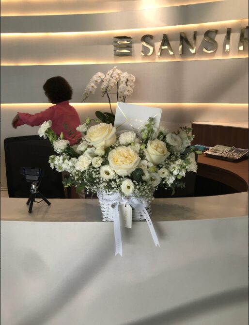 Luxury white flower basket with roses, carnations, daisies, baby’s breath, and eucalyptus, decorated with ribbon.