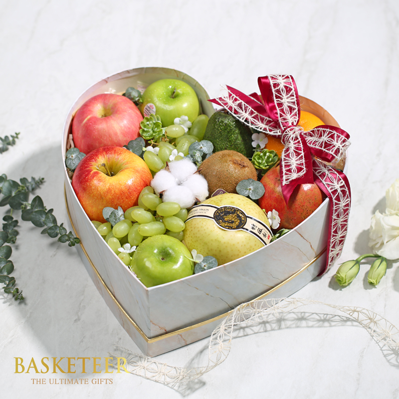 Mixed oranges, apples, Kiwis, avocados, golden Pears and grapes in a heart box with bow