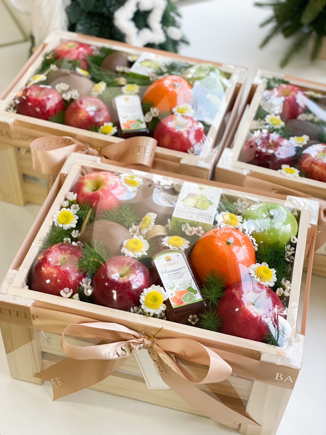 Wooden fruit crate with apples, oranges, and kiwis, decorated with flowers and a bottle of lime honey, wrapped in a satin Basketeer ribbon.