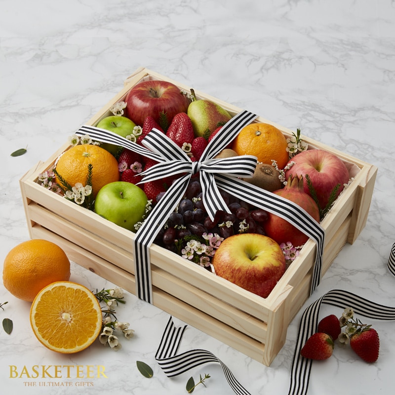 A lavish wooden crate brimming with an exquisite selection of handpicked fruits, including juicy apples, vibrant oranges, succulent strawberries, and luscious grapes. The arrangement is elegantly adorned with delicate white blossoms that elevate its charm. A stylish black-and-white striped ribbon and bow provide a sophisticated accent. The 