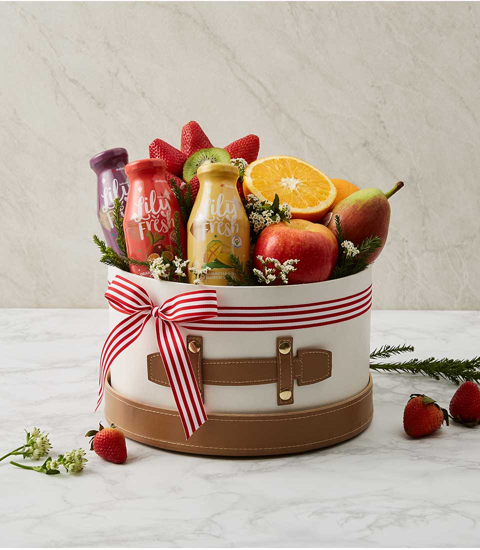 A white gift box with brown edges filled with a variety of fresh fruits such as red strawberries, healthy drinks, and more. Decorated with a red ribbon bow with white lines.