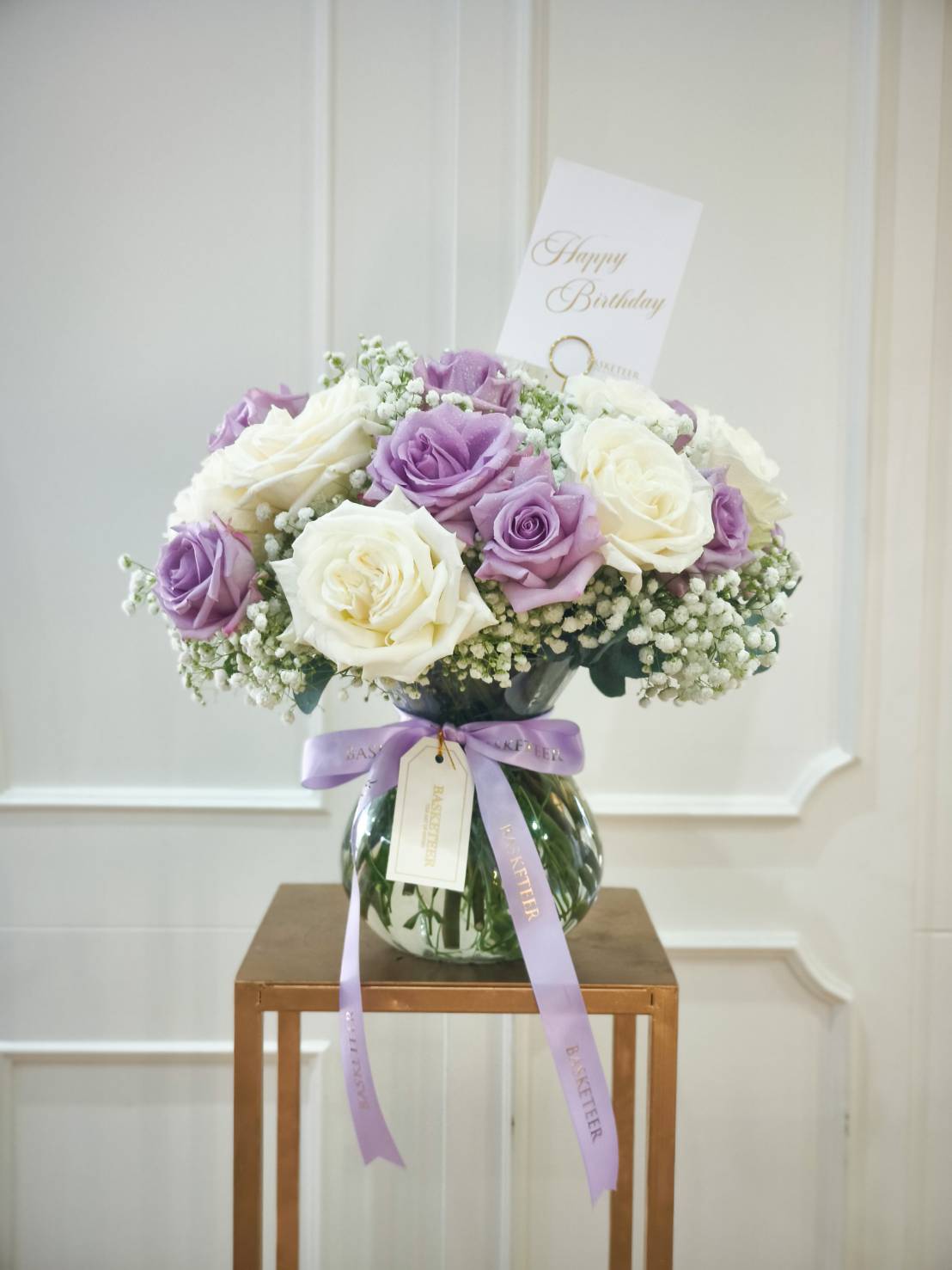 Elegant glass vase with white and lavender roses, accented with baby’s breath and tied with a lavender ribbon.