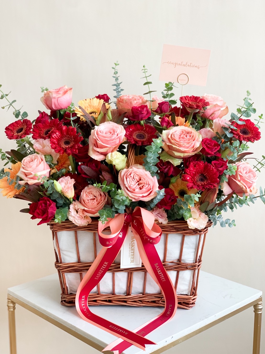 Congratulations flower basket with pink and red roses, gerberas, and lush foliage.