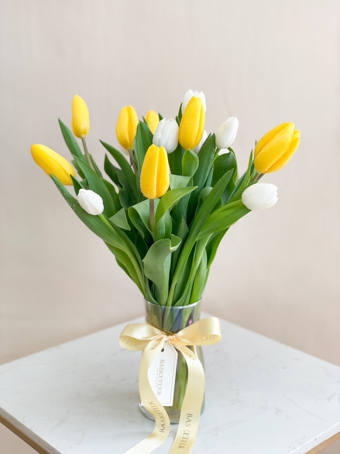 A fresh tulip arrangement with yellow and white tulips in a glass vase, tied with a golden satin ribbon.