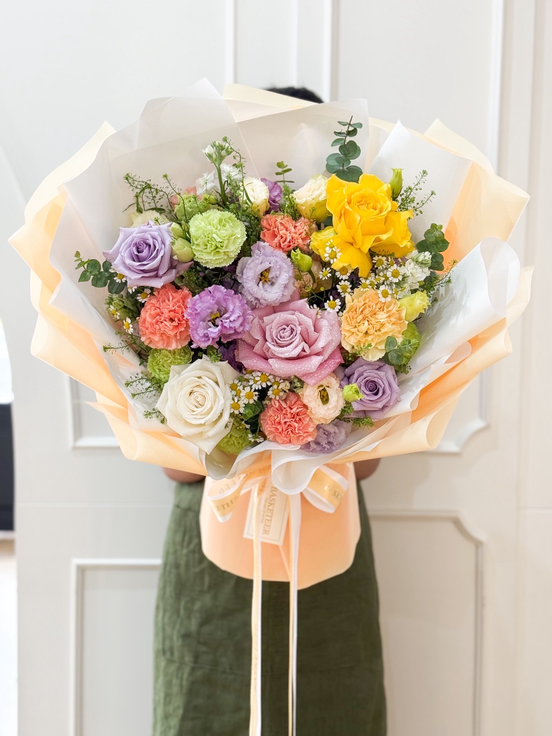 Luxurious pastel bouquet with roses, carnations, eustomas, and chamomile wrapped in soft yellow and white paper