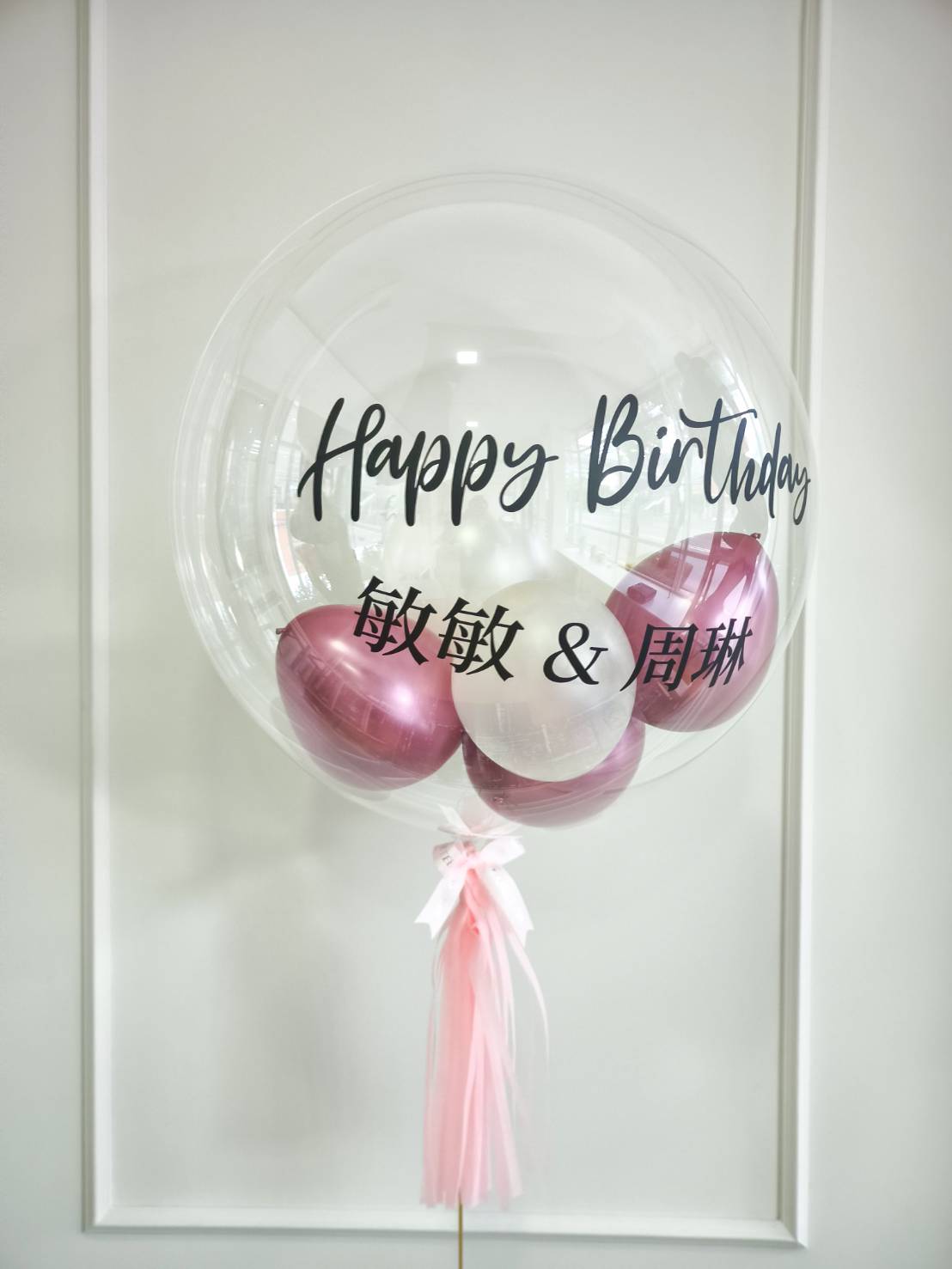 Transparent bubble balloon with personalised Happy Birthday message in black text, filled with pink and white balloons.