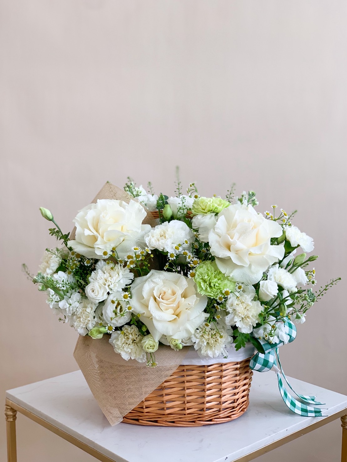 Elegant flower basket arrangement with white roses, carnations, and green accent flowers in woven basket.