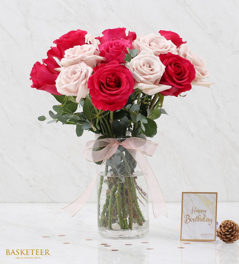 A luxurious bouquet of vibrant red and delicate light pink roses graces an elegant clear glass vase, adorned with a charming pink ribbon. The exquisite arrangement rests on a pristine marble surface, accompanied by a chic 