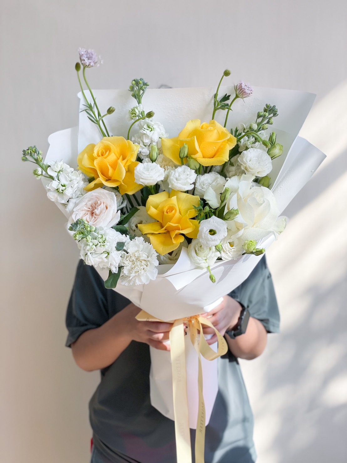A fresh yellow and white rose bouquet wrapped in elegant white paper, symbolizing joy, friendship, and new beginnings.