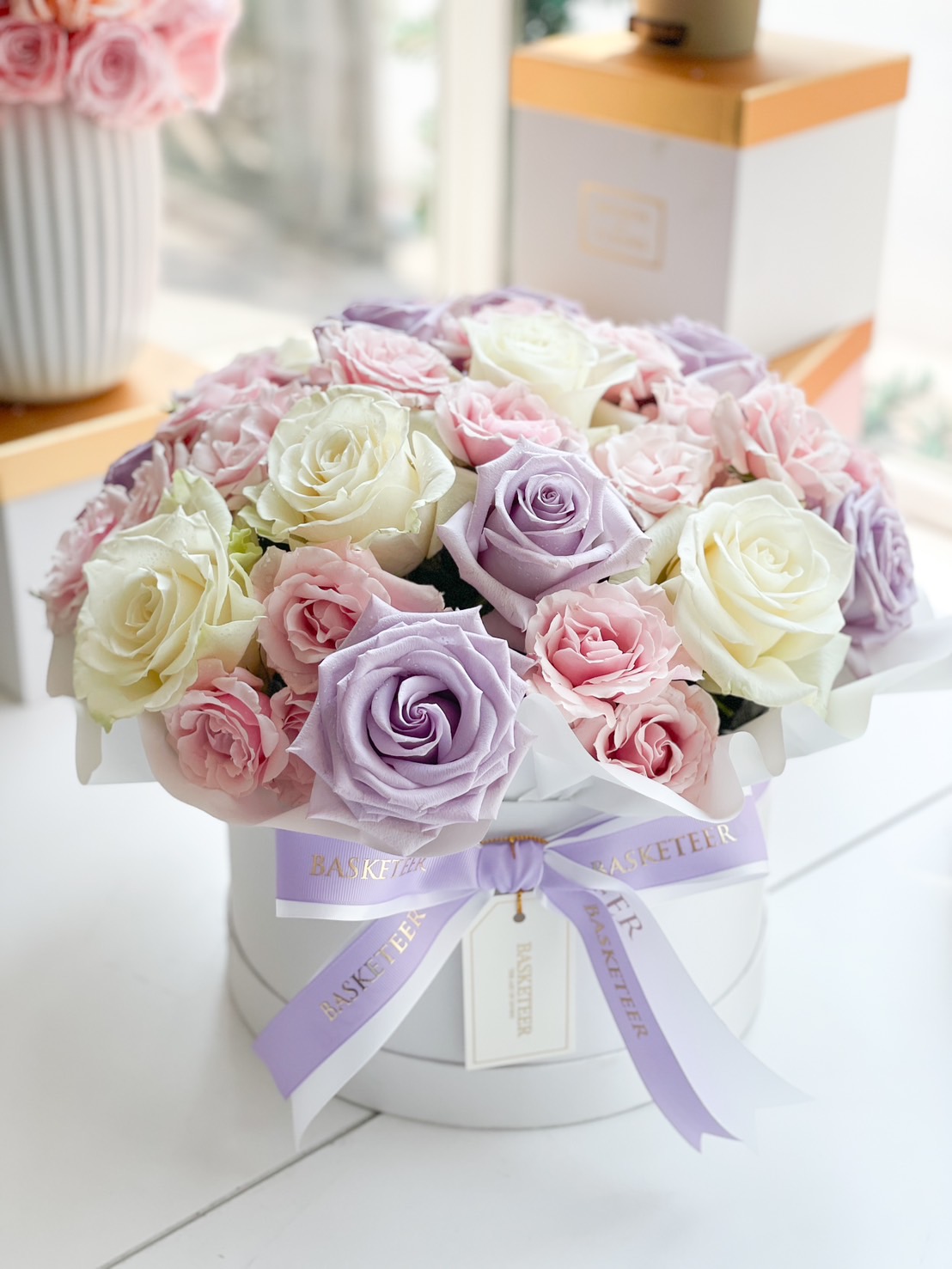 A beautifully arranged pastel rose box with lavender, white, and pink roses, wrapped in an elegant white gift box with a satin ribbon.