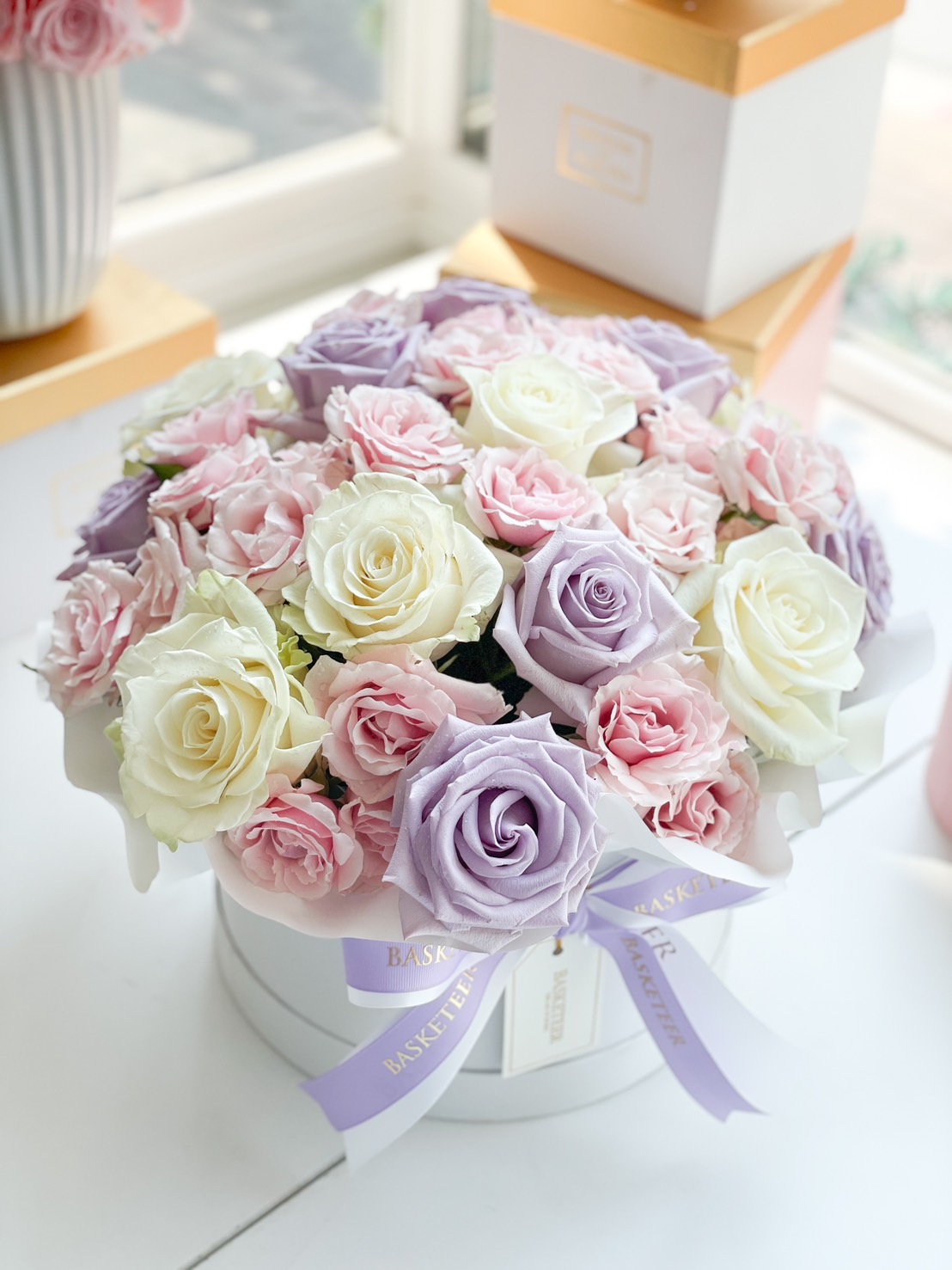 A beautifully arranged pastel rose box with lavender, white, and pink roses, wrapped in an elegant white gift box with a satin ribbon.