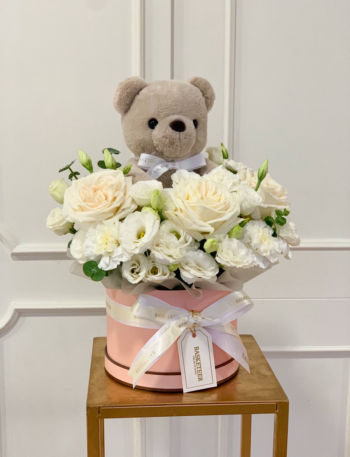 Cream and white flower box with roses, lisianthus, and a plush teddy bear in a pink hatbox