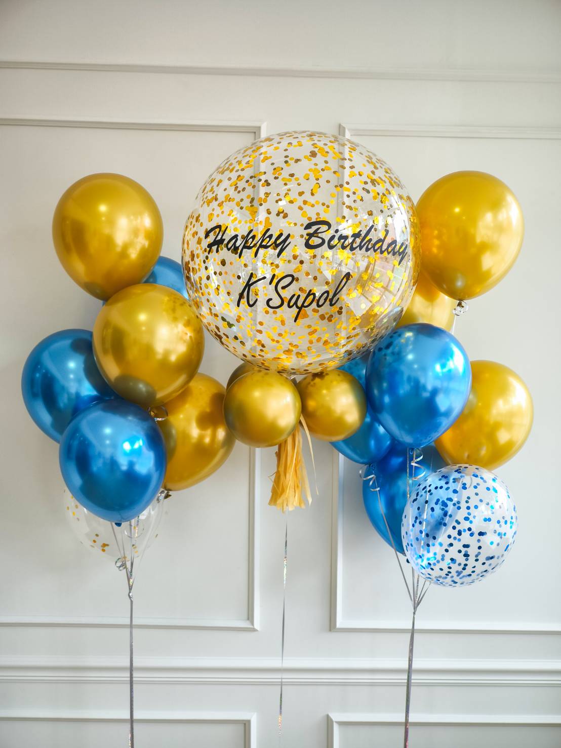 Birthday balloon set in gold and blue tones, featuring a large transparent balloon with gold confetti and personalized text.