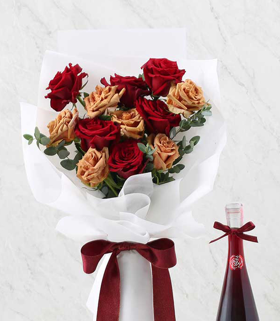 A bouquet of red and peach roses wrapped in white paper with a deep red ribbon sits in a clear vase. Beside it, the elegant Wine & Red Flower Combo includes a 