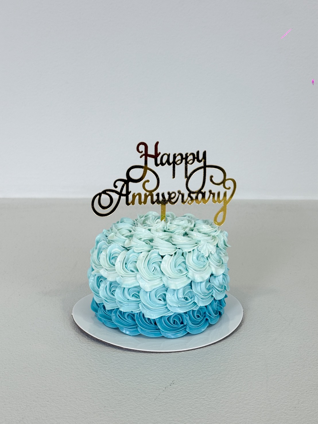 A small round sky blue cake with blue and white swirled icing, topped with a decorative 