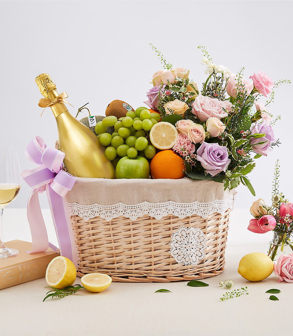 Elegant fruit and flower basket with golden sparkling bottle, green grapes, apple, citrus, and pastel roses