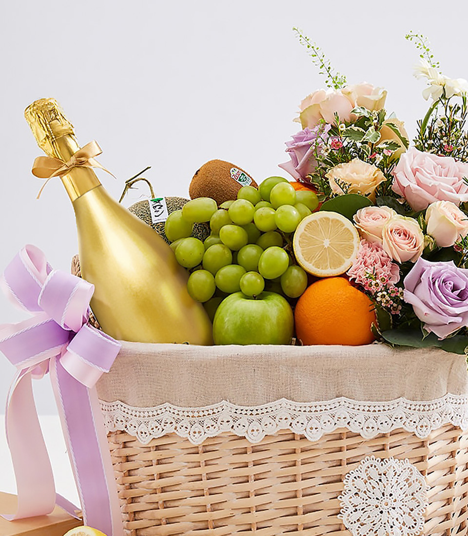 Luxury gift basket with golden sparkling wine, green grapes, apple, citrus, kiwi, and pastel flowers