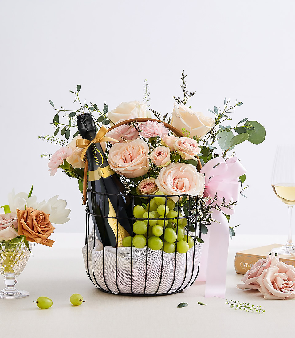 Elegant gift basket with Bottega sparkling wine, green grapes, and pastel roses in a black wire basket