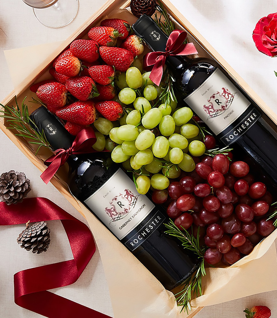 Close-up of gift box with two bottles of Rochester red wine, strawberries, green grapes, red grapes, and rosemary sprigs