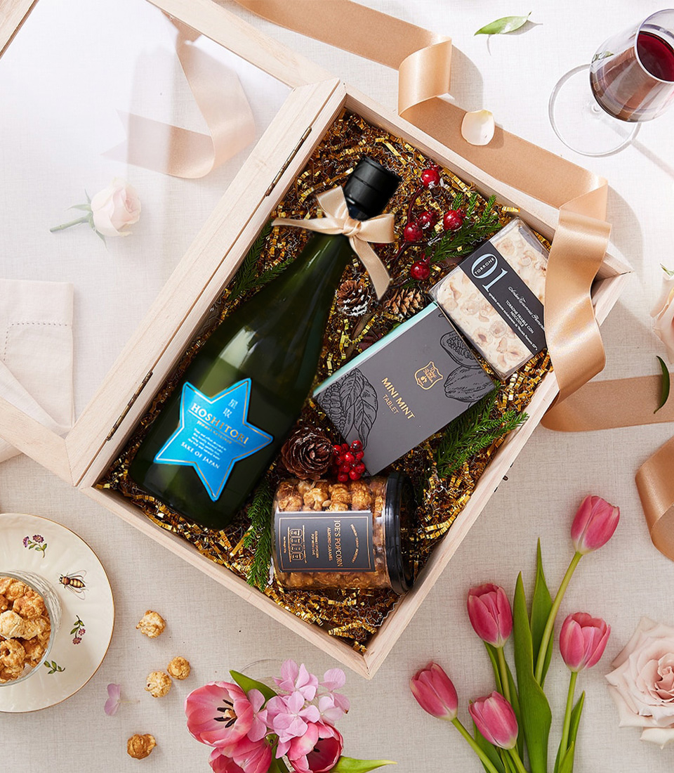 A beautifully curated gourmet gift box featuring a bottle of Hoshitori Japanese sparkling wine, premium caramel popcorn, artisan nougat, and mini mint dark chocolate in an elegant wooden box with a clear lid and gold ribbon.