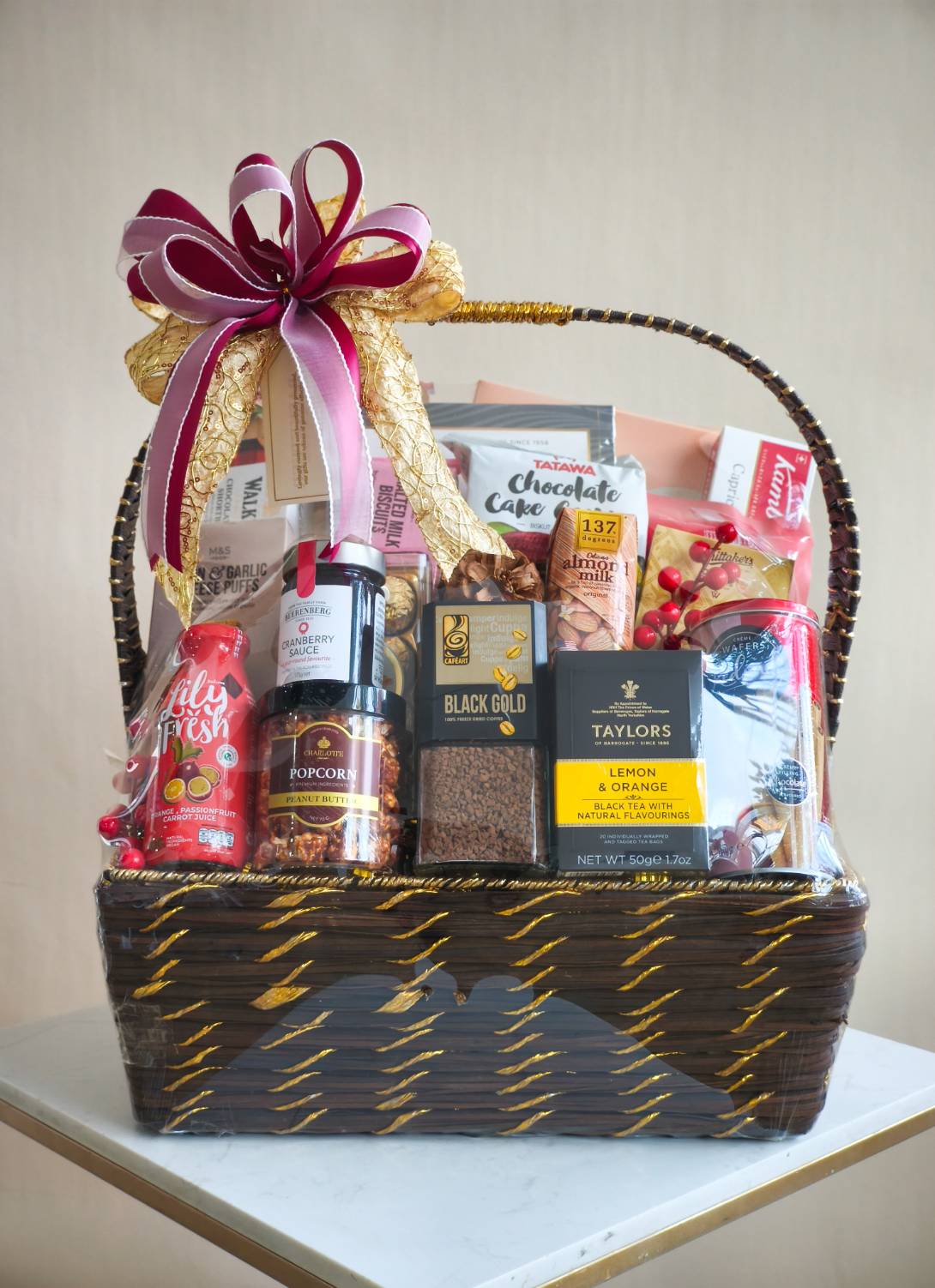 Luxury gift basket with assorted premium snacks, tea, coffee, juice, cookies, and cranberry sauce, wrapped with a gold and burgundy ribbon.