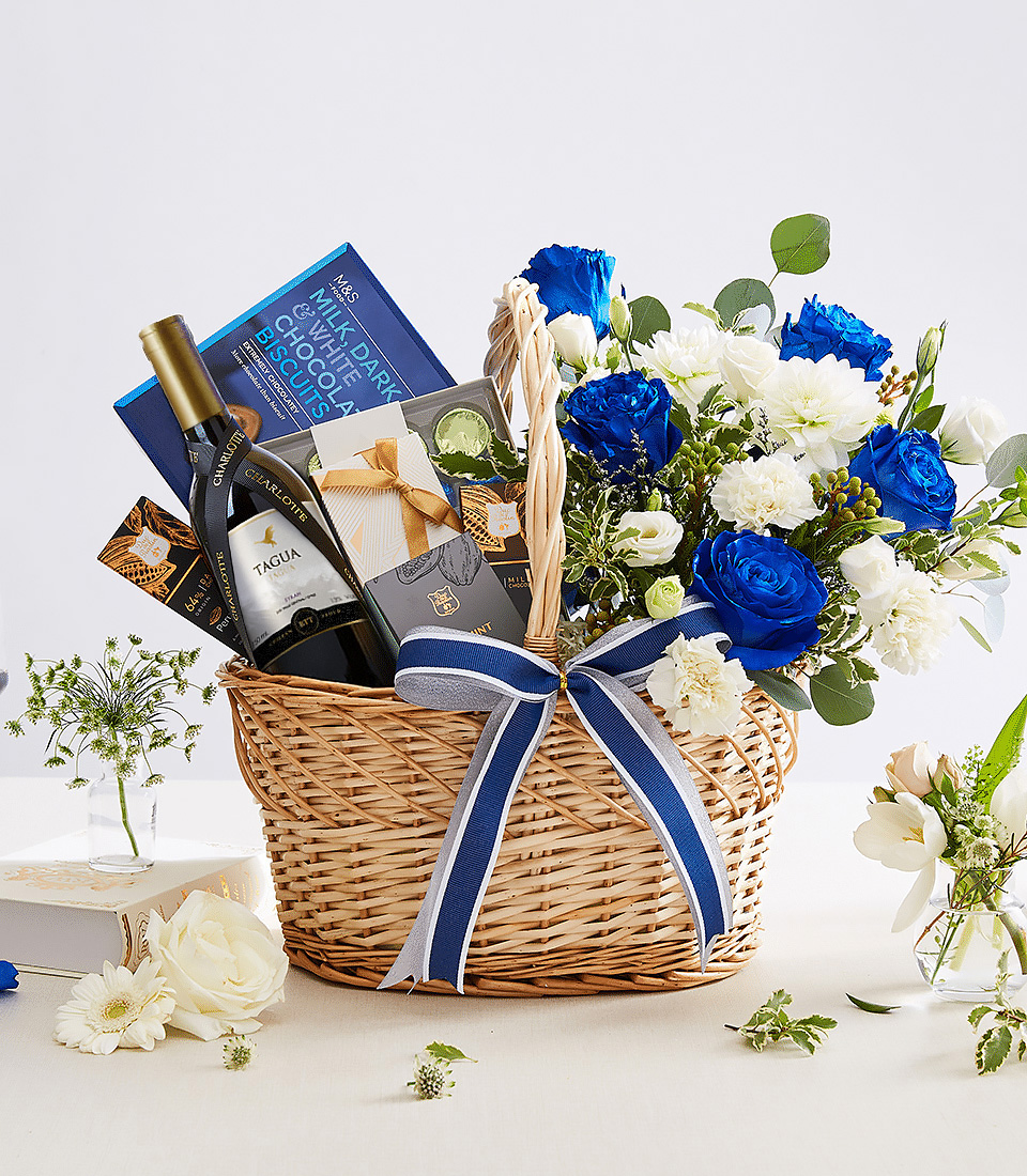 A luxury gift basket featuring a bottle of fine white wine, gourmet chocolates, and premium biscuits, elegantly arranged with vibrant blue and white flowers in a woven basket adorned with a navy blue ribbon—perfect for corporate gifting, anniversaries, and celebrations.