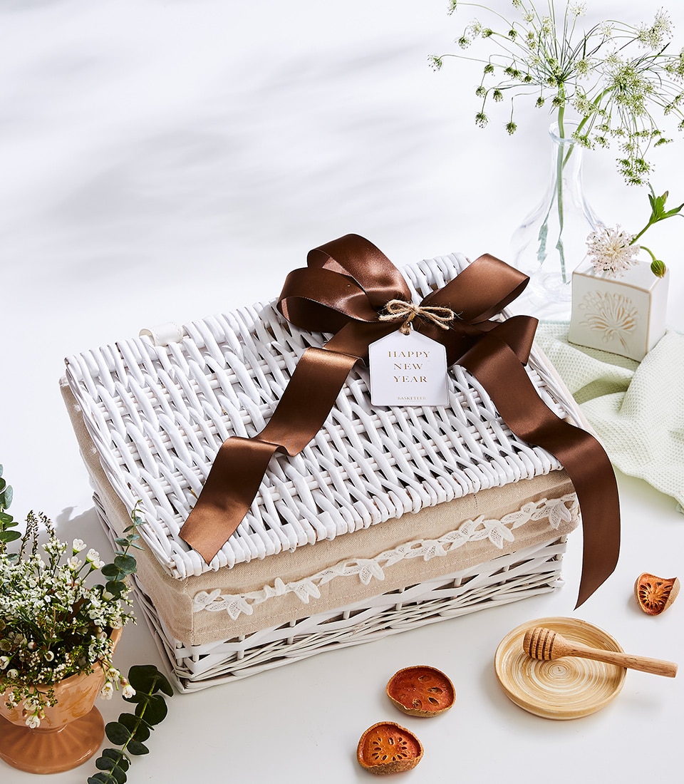 A luxurious white wicker gift basket, embellished with a rich brown ribbon and adorned with a 