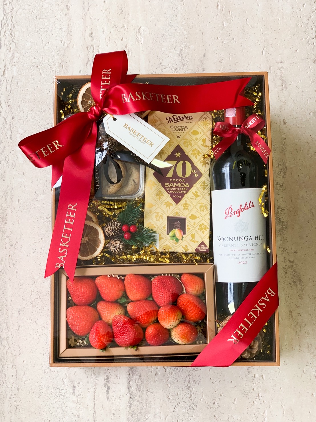 Luxury gift box with Penfolds red wine, fresh strawberries, dark chocolate, and festive decorations tied with a red ribbon