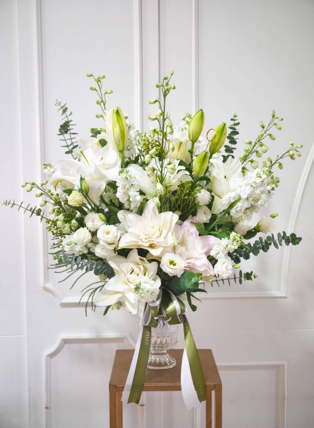 Luxury tall vase with white lilies, roses, lisianthus, and lush greenery, styled with elegance and Basketeer ribbon.