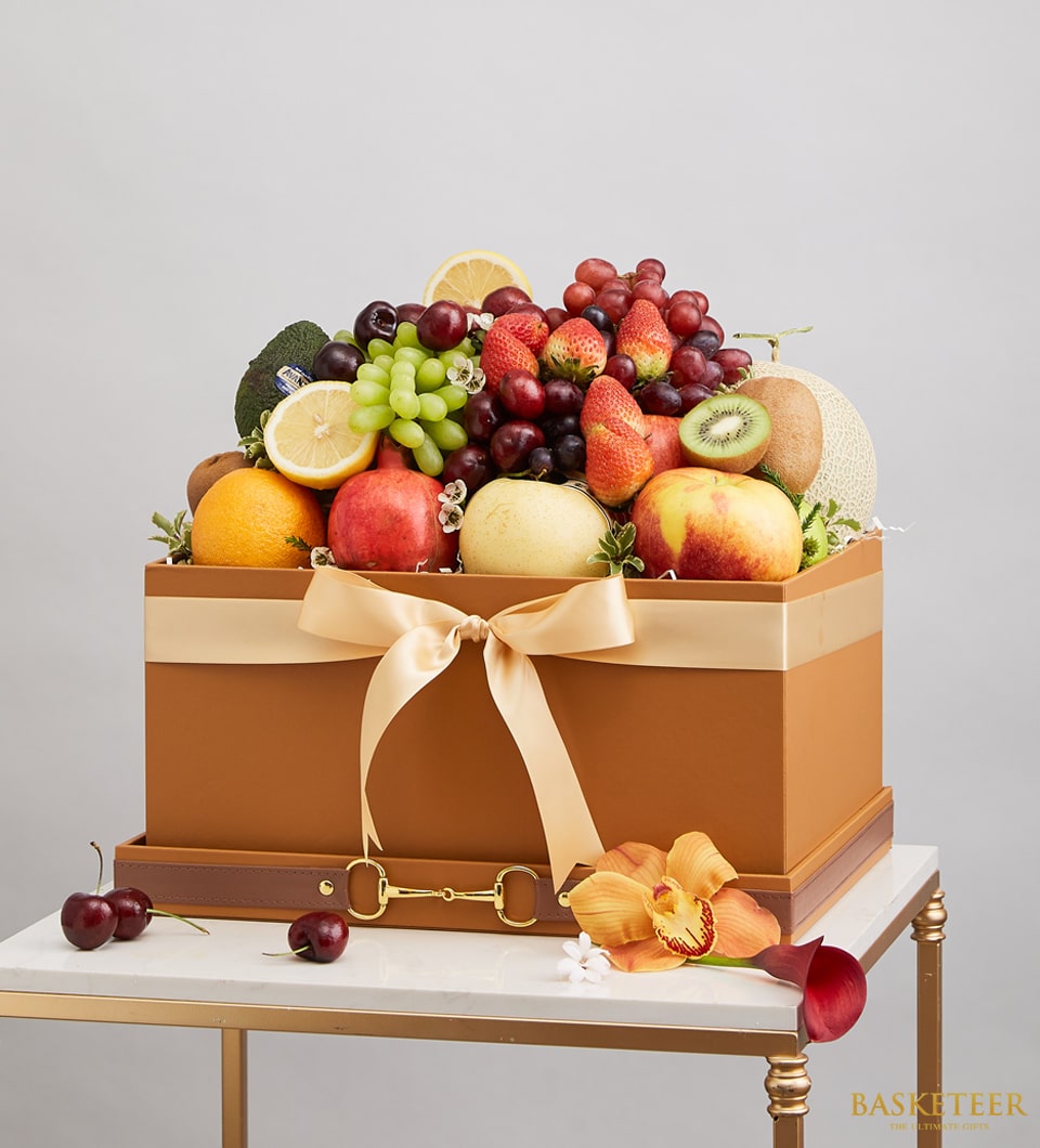 A lavish gift box brimming with an exquisite selection of fresh fruits, including succulent apples, grapes, strawberries, melon, and oranges. Elegantly adorned with a satin ribbon bearing the esteemed 