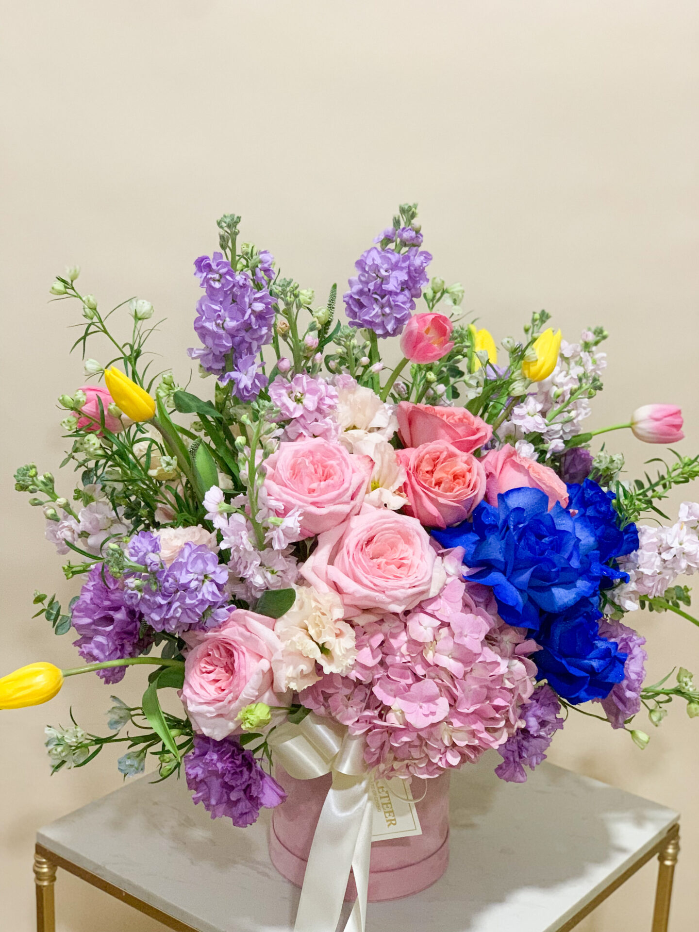 A lavishly curated floral arrangement presented in a chic, pastel-colored vase adorned with the elegant word 