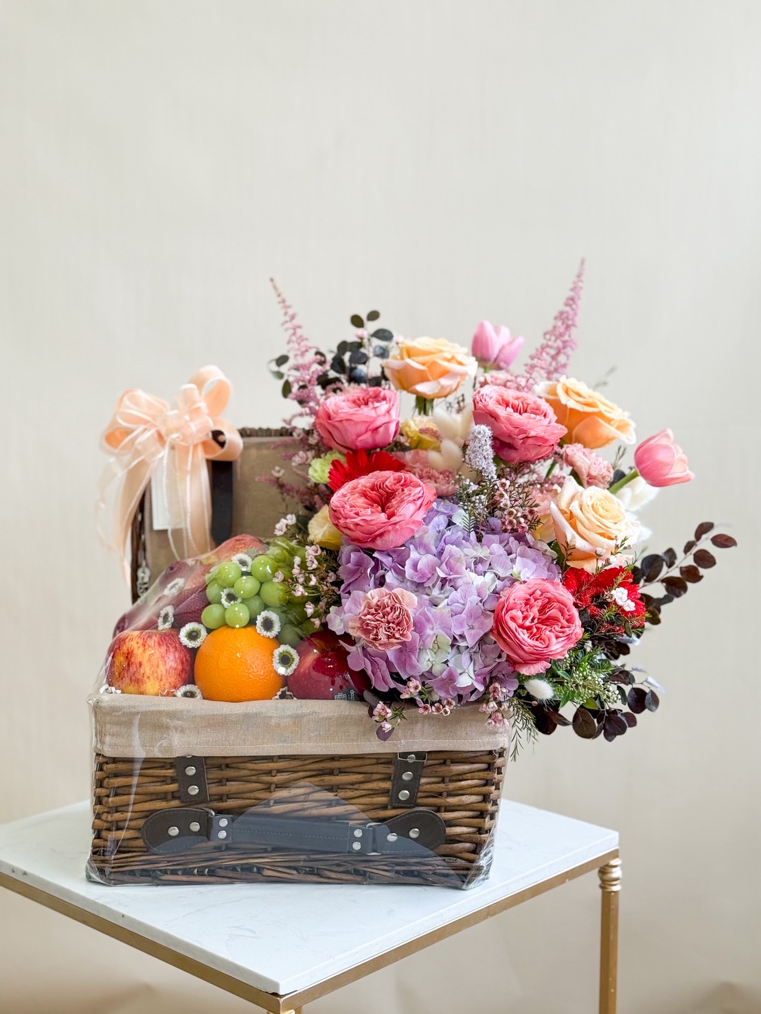 Premium wicker hamper filled with apples, grapes, and oranges, paired with a vibrant arrangement of roses, hydrangeas, and tulips.
