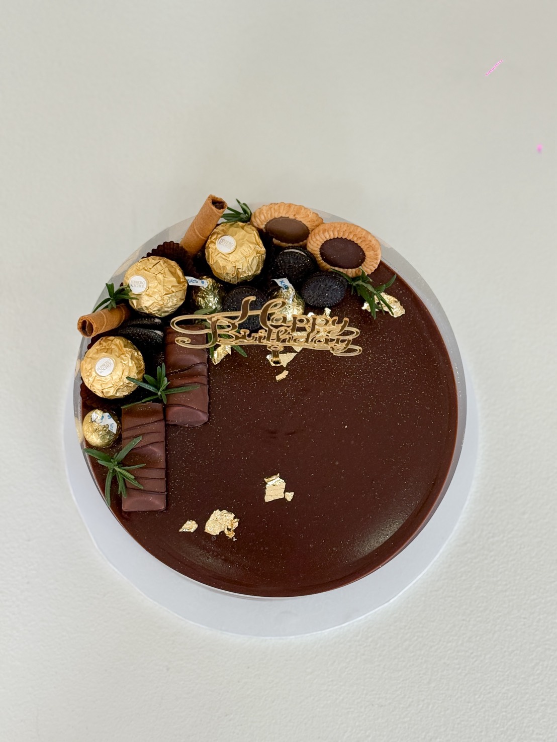 Luxury chocolate cake decorated with Ferrero Rocher, cookies, chocolate bars, wafer rolls, and edible gold leaf, with Happy Birthday topper