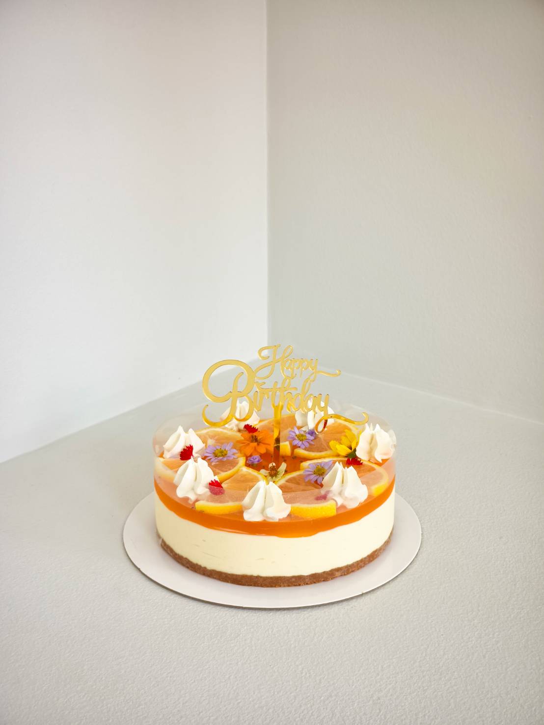 Fresh orange citrus cheesecake topped with whipped cream, fruit slices, and edible flowers, perfect for birthdays.