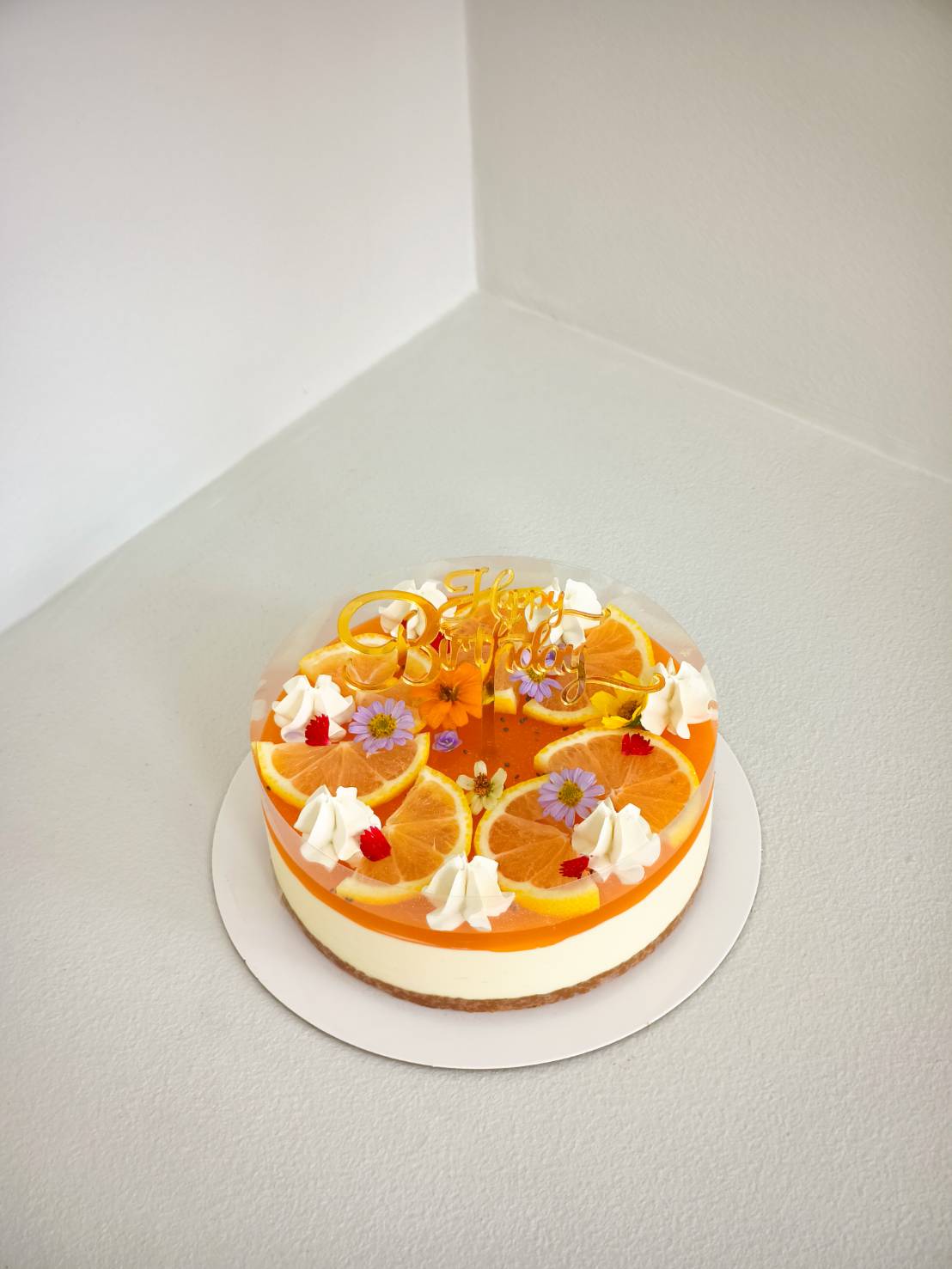 Fresh orange citrus cheesecake topped with whipped cream, orange slices, and edible flowers for birthdays.
