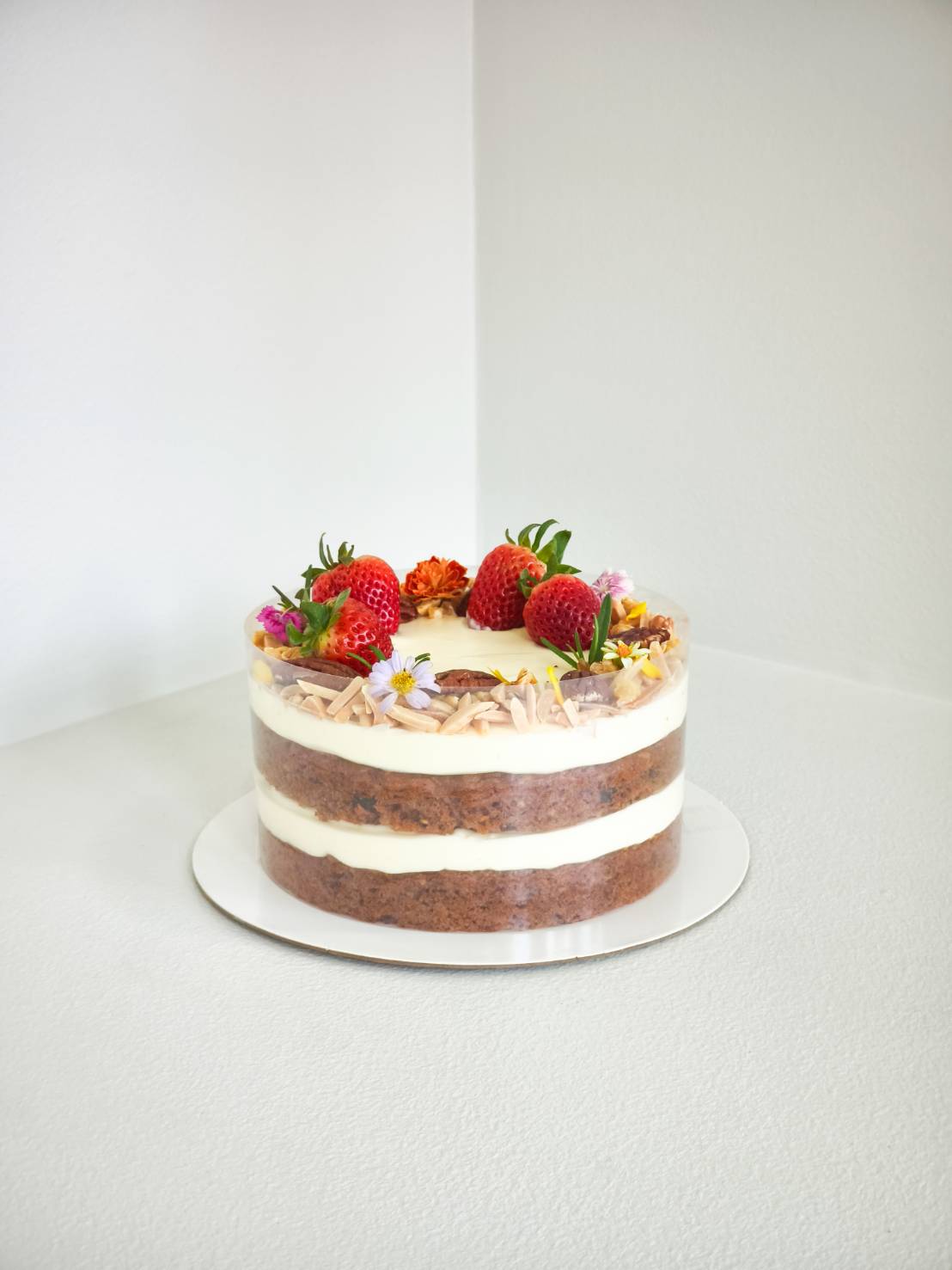 Three-layer naked cake with cream cheese filling, topped with fresh strawberries, almonds, and edible flowers.