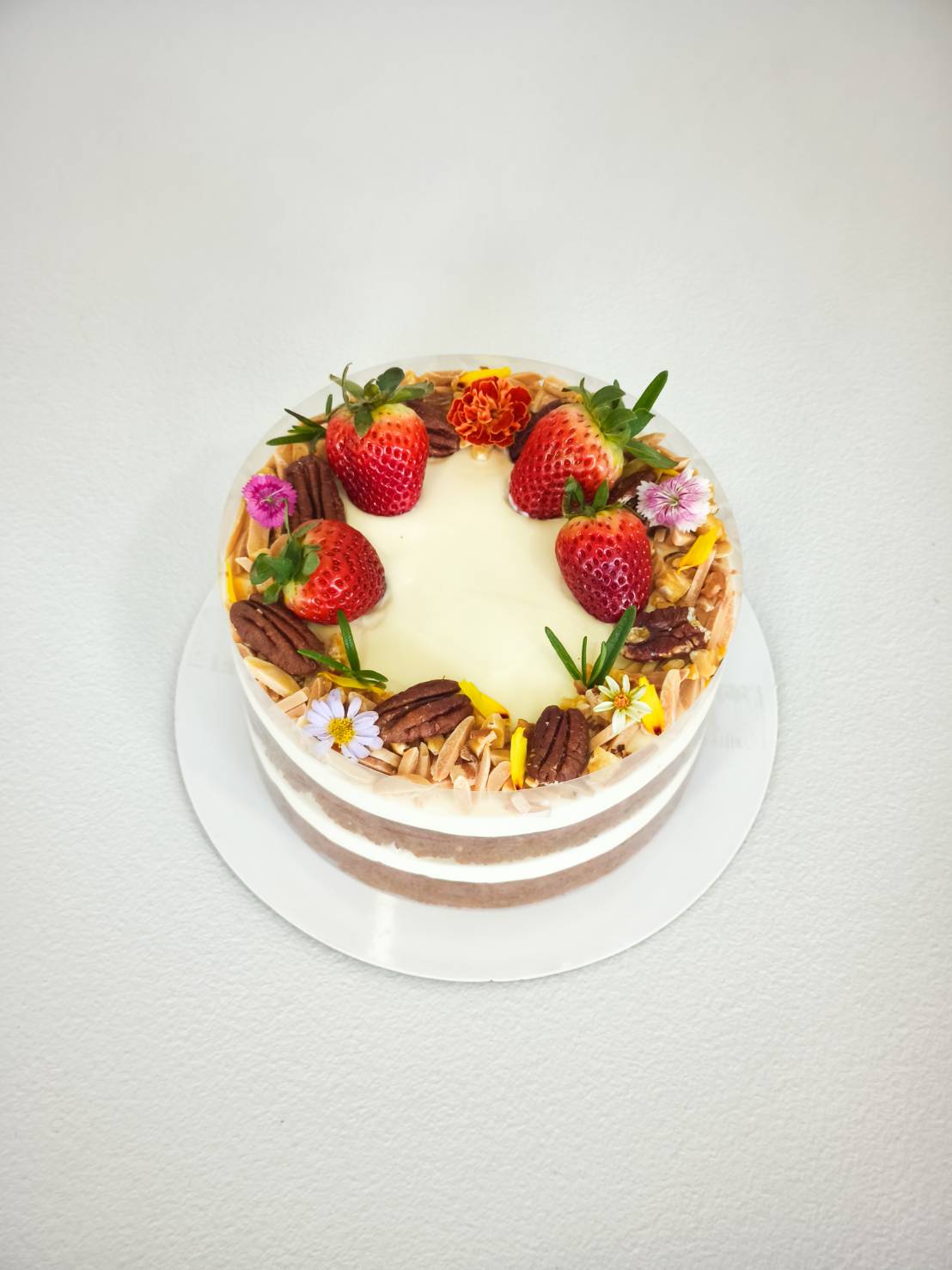 Naked cake with cream cheese filling, topped with fresh strawberries, pecans, almond flakes, and edible flowers.