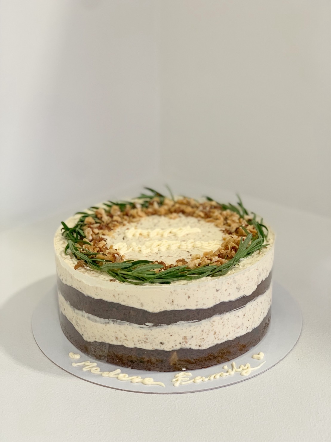 Carrot walnut naked cake with cream cheese frosting layers, rosemary and crushed walnut topping.