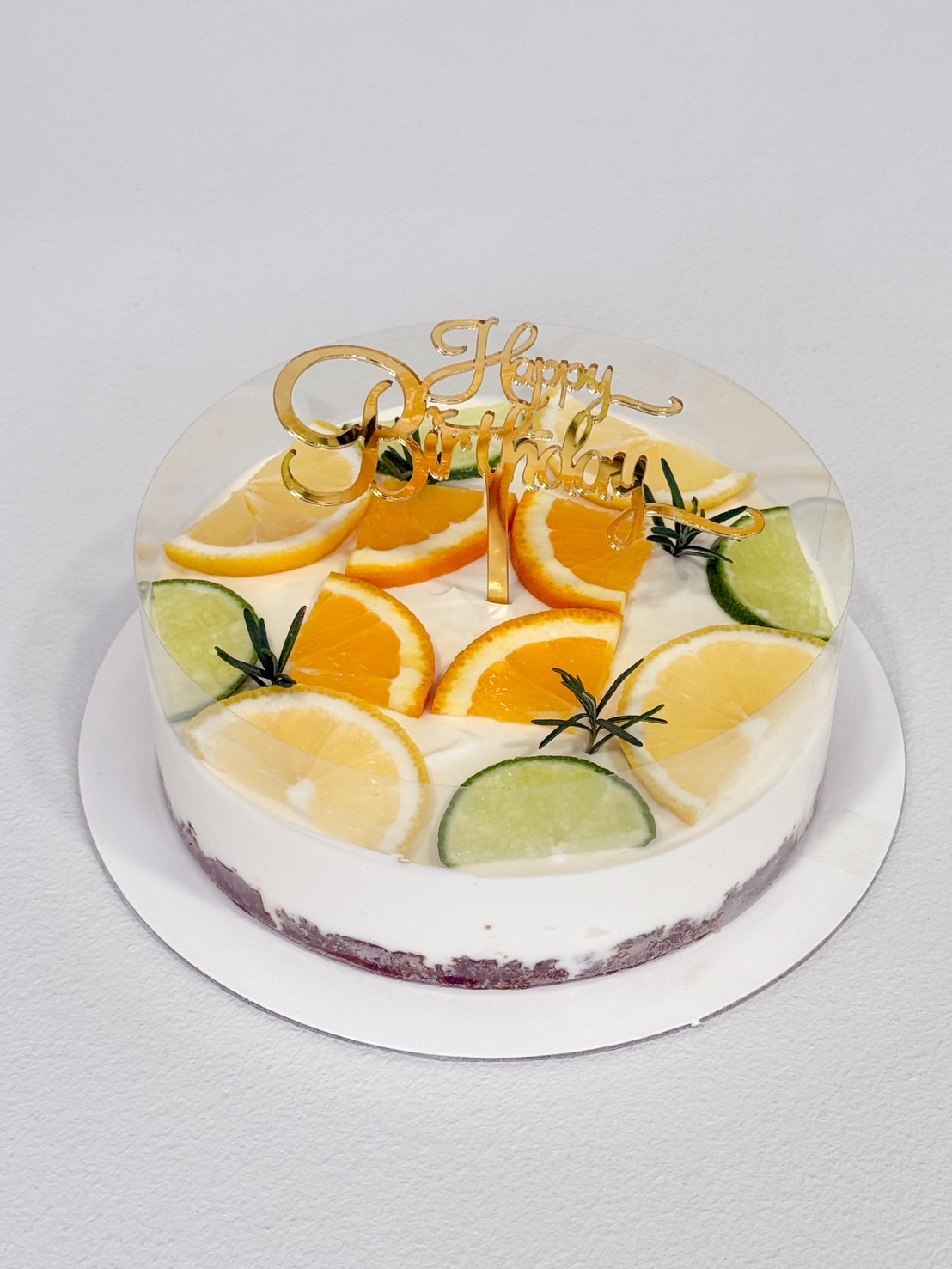 Citrus yogurt cheesecake topped with fresh orange, lemon, and lime slices, decorated with rosemary and Happy Birthday topper.