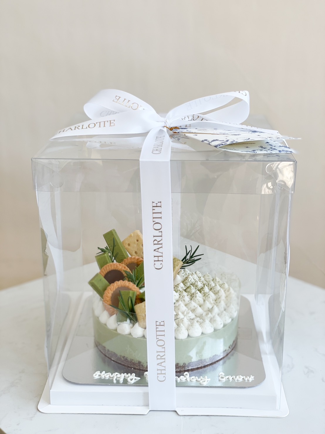 A beautifully packaged Matcha cheesecake, topped with whipped cream, matcha dust, and elegant garnishes, wrapped in a luxury gift box.